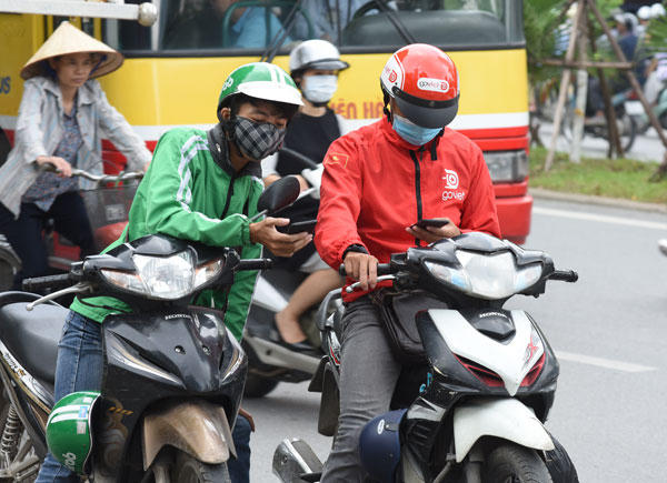 Tài xế Grab và Go-Viet đứng dưới lòng đường chăm chú nhìn điện thoại tìm khách (Chụp trên đường Nguyễn Chí Thanh, Hà Nội) - Ảnh: Khánh Linh