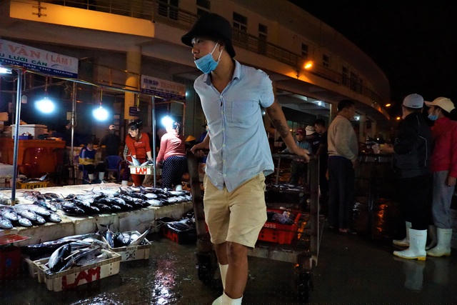 Dưới ánh đèn vàng hắt ra từ những vựa thu mua hải sản bên cạnh, có thể nhìn rõ vẻ ngái ngủ trên gương mặt nhiều người. Nhưng với họ, việc mưu sinh vẫn là ưu tiên số một. Những thanh niên bốc vác cá vội vàng nhận cá từ thương lái rồi lại hối hả vận chuyển ra xe để kịp giờ đến chợ. Dường như, ai cũng sợ chỉ cần chậm chân một chút, thì thu nhập của một ngày làm việc của họ sẽ giảm.
