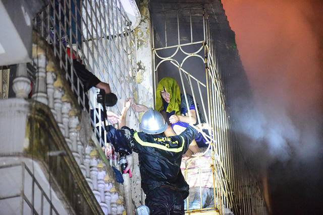 Từ nhà bên cạnh, cảnh sát PCCC cắt sắt để tiếp cận sang tầng trên cùng của ngôi nhà cháy. Tới 4h sáng, nạn nhân đầu tiên được đưa ra khỏi đám cháy.