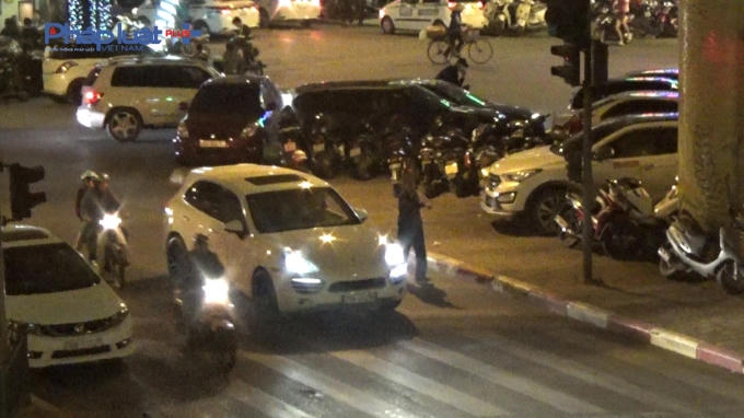 Người đàn ông đang hướng dẫn xe ô tô màu trắng đậu vào lòng đường, xung quanh là nhiều xe ô tô khác đang được trông giữ.