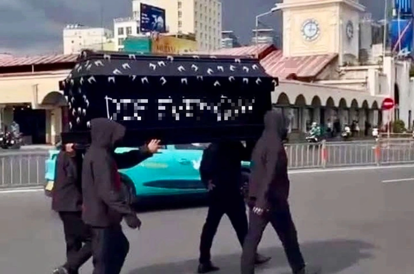 Nhóm 4 người mặc đồ đen, trùm đầu, khiêng quan tài trước chợ Bến Thành.