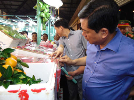 Bí thư Thành ủy TP.HCM (bìa phải) đang xem nhãn mác trái cây nhập từ Trung Quốc bán tại chợ đầu mối Thủ Đức. Ảnh: LÂM NGỌC