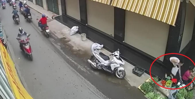 Người phụ nữ áo trắng đang cuois xuống lấy trộm túi tiền của bà bán rau. Ảnh cắt từ clip.