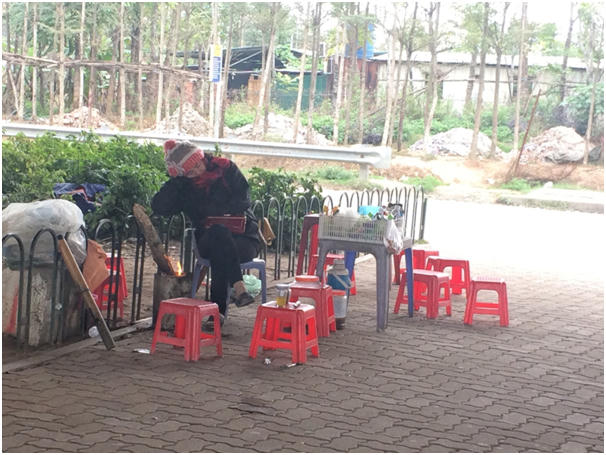 Chị chủ quán nước ven đường gần Khu công nghiệp Thăng Long đang co ro bên bếp lửa.