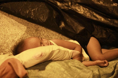 Đứa bé nằm ngủ trên ghế đá với tấm chăn mỏng manh và quần áo rách tả tơi.