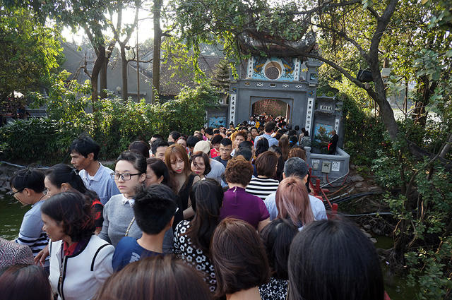 Đền Ngọc Sơn (Hà Nội) mở cửa từ 7 giờ sáng đến 18 giờ hàng ngày. Tuy nhiên, lượng người tập trung đông nhất trong khoảng từ 10h đến 16h. Hàng nghìn lượt khách “gói gọn” trong giờ vàng đã tạo ra cảnh đông đúc, chen lấn đến nghẹt thở. Trong ảnh là cảnh hàng đoàn người chen nhau chật cứng tại lối dẫn vào cổng đền.