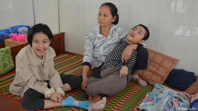 Người mẹ đang phải chăm sóc hai đứa con bị di chứng chất độc da cam. Ảnh: dw.com