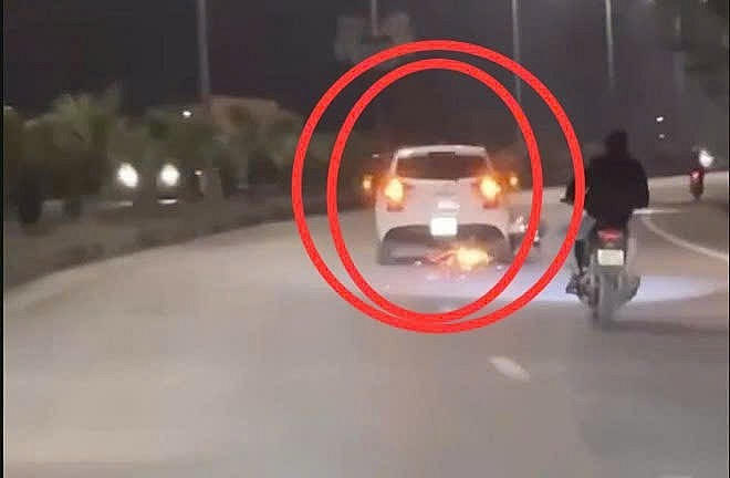 Hình ảnh chiếc ô tô kéo lê chiếc xe máy "đánh lửa" nhiều km trên đường khiến nhiều người bức xúc. (Hình ảnh cắt từ clip.)