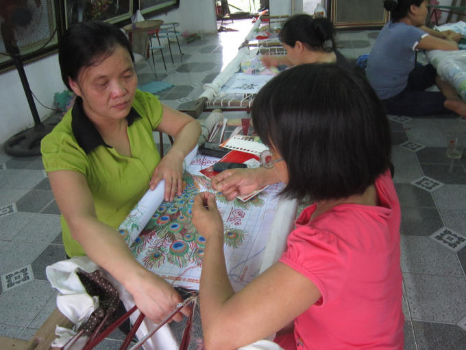Chị Khương đang chăm chú nhìn nhân viên của mình thêu tranh.