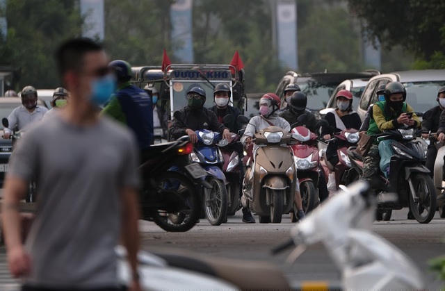 Một người đi thể dục trên đường đi bộ dọc bờ sông Tô Lịch, phía sau rất đông phương tiện xe máy, ô tô đứng đợi đèn đỏ.