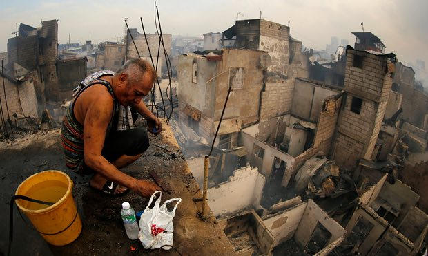 Một người d&acirc;n thu lượm những đồ đạc vẫn c&ograve;n sử dụng được sau đ&aacute;m ch&aacute;y. (Ảnh: EPA)