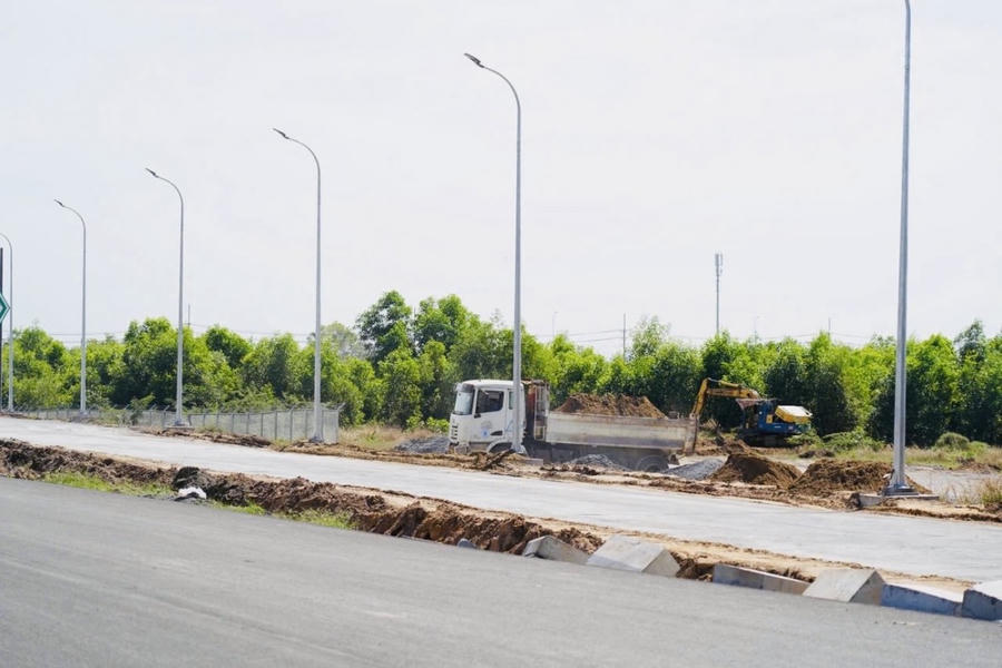 Công nhân và máy móc đang gấp rút thảm nhựa mặt đường, lắp đặt hệ thống chiếu sáng, dải phân cách và biển báo an toàn giao thông.