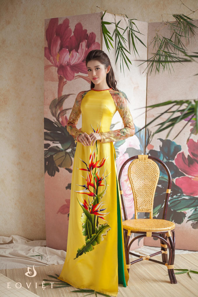 Màu vàng là gam màu khó mặc nhất, tuy nhiên với thiết kế cổ tròn cùng với đường viền đỏ ở cổ và sự phá cách ở 2 tà cánh tay đã khiến chiếc áo dài “kén người mặc” mấy cũng trở nên mềm mại, dễ mặc hơn. Họa tiết hoa màu đỏ làm cho tông vàng trở nên dịu nhẹ hơn.
