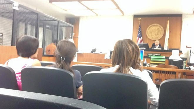 Minh Béo đứng trong lồng sắt, cúi đầu và nép sau người phiên dịch, luật sư. Ảnh: Thiện Thành.