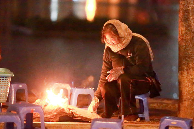 Một người b&aacute;n nước b&ecirc;n đường đang đốt lửa sưởi ấm ngo&agrave;i trời gi&oacute; r&eacute;t.