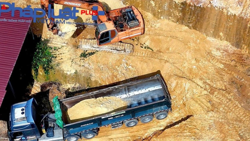 Máy xúc đang hối hả xúc đất lên xe đầu kéo.