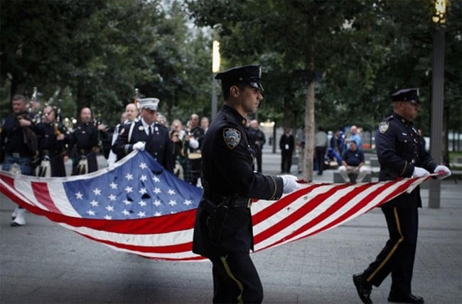 Sáng sớm 11/9/2015, thành viên lực lượng cảnh sát New York rước quốc kỳ Mỹ tại khu tưởng niệm các nạn nhân vụ tấn công khủng bố 11/9/2001. (Ảnh: AFP)