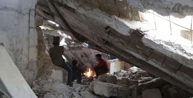 Những bé trai sưởi ấm bên đống lửa dưới một toà nhà đổ nát tại tỉnh Idlib, Syria, ngày 29/12/2015. Ảnh: Reuters.