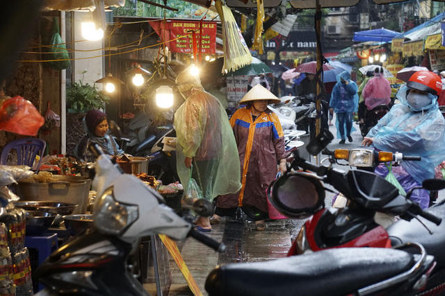 xCác bà nội trợ trùm kín áo mưa đi chợ với lỉnh kỉnh các loại túi đựng thực phẩm, rất bất tiện.