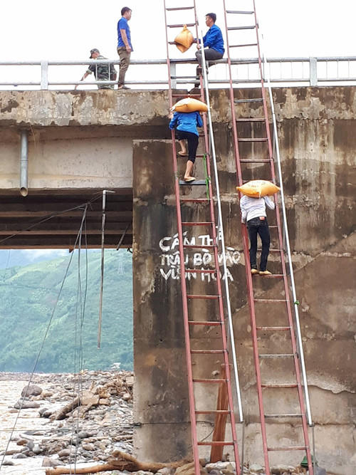 Từ lòng suối lên mặt cầu cao hàng chục mét, thanh niên vừa cõng gạo, vừa phải leo thang.