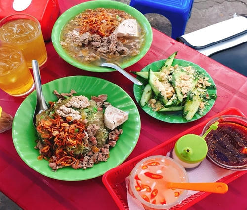 Chủ quán thong thả trụng bánh đa, miến, rau… vào nồi nước dùng vàng màu cua cho khách, sau đó thêm thịt bò, chả cá, giò, nước trộn, hành phi, lạc rang. Đĩa dưa chuột muối ăn kèm tạo cảm giác bớt ngán. Ngoài đồ trộn, quán cũng phục vụ thêm các món nước. Phần ăn đầy đặn, hương vị đậm đà, giá một phần cơ bản là 25.000 đồng, các phần có thịt bò, giò… thường là 45.000 đồng. Thực khách phải gửi xe ở phía đối diện, giá 2.000 đồng. Theo nhiều thực khách, ai đi ăn ở đây phải có sự kiên nhẫn, bởi quán đông khách và phục vụ hơi chậm, nhất là khi gọi thêm đồ. Quán bán từ 11h trưa đến tối. Ảnh: lozi.