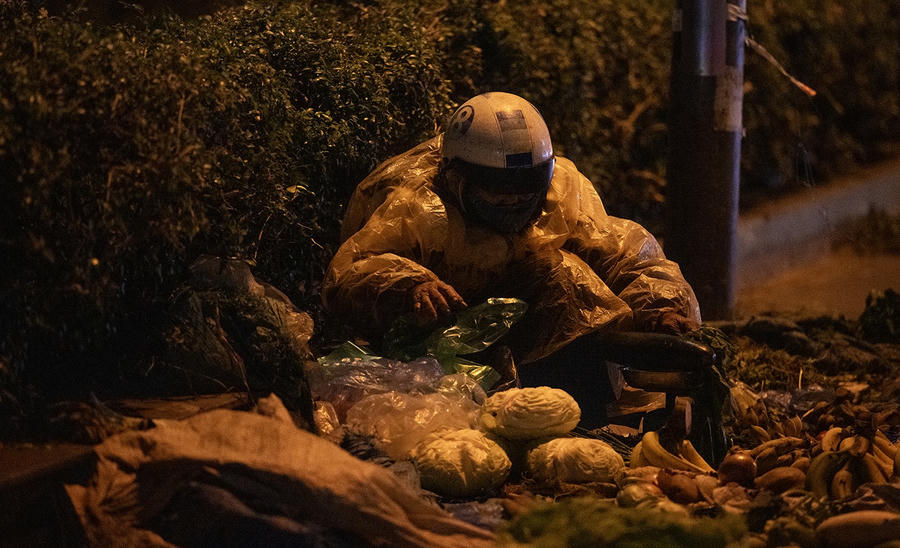 Một cụ già phải mặc áo mưa để giữ ấm bán hàng rau củ quả trên đường Hồ Tùng Mậu.