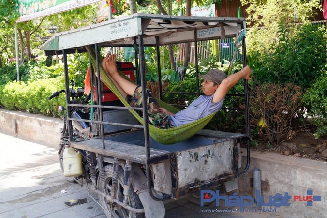 Một tài xế xe 3 bánh nghỉ trưa dưới  bóng râm hiếm hoi.