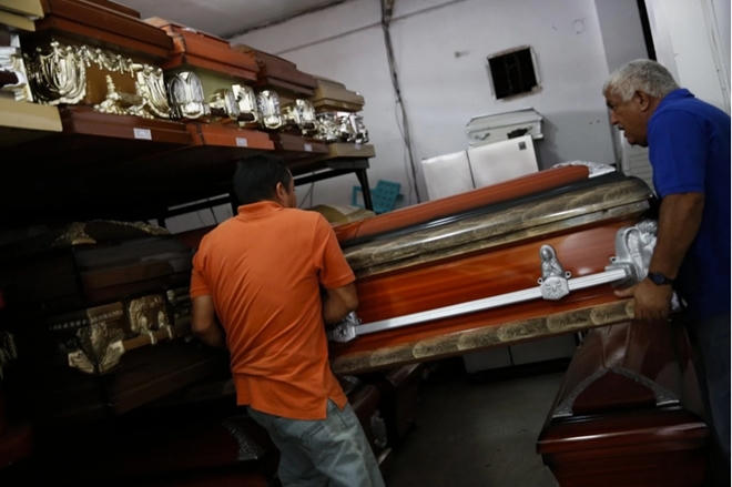 Hai công nhân khuân một quan tài ra khỏi nhà kho tại thủ đô Caracas trong năm 2014. Ảnh: Reuters