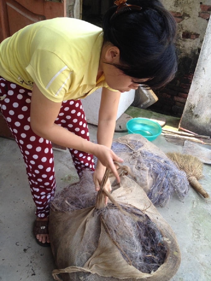 Chị Hằng, vợ anh Quang Anh đang buộc lại đống lưới dính đầy rác va phải cọc vây trên biển bị rách bươm, vứt một chỗ từ mấy tháng nay. Ảnh: Trung Du.