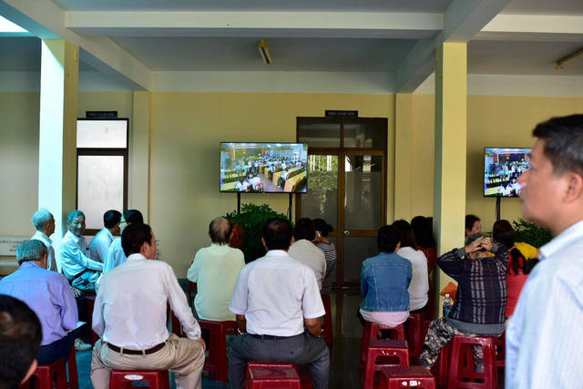 Một số người dân ngồi ngoài cửa hội trường theo dõi buổi công bố kết luận qua ti vi