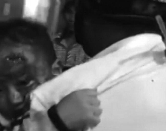 Cháu bé với vết thương trên trán và máu chảy ướt vai người cha. (Ảnh cắt từ Clip)