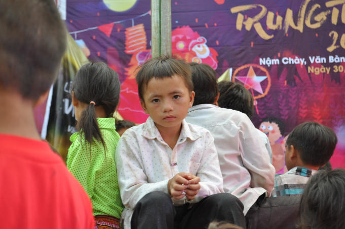 Một em học sinh lớp tiểu học ngồi dưới sân trường cùng các bạn chờ đến tối để đón Trung Thu.