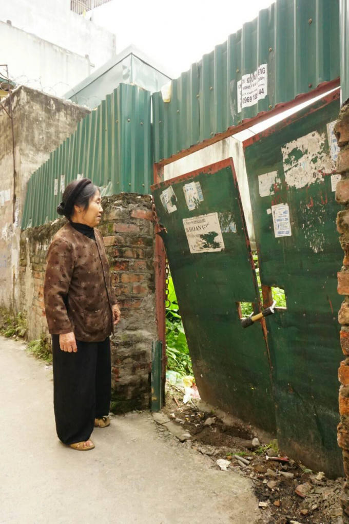 Bà Lưu Thị Dong đứng trước khu vườn bị chặt phá và đang bị cô Bưởi đóng cửa lại.