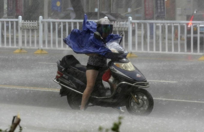 Một cô gái mặc áo mưa và đội mũ bảo hiểm để chống lại cơn mưa xối xả tạt vào mặt do ảnh hưởng của bão Rammasun vào tỉnh Quảng Đông, Trung Quốc năm 2014. (Ảnh: Reuters)