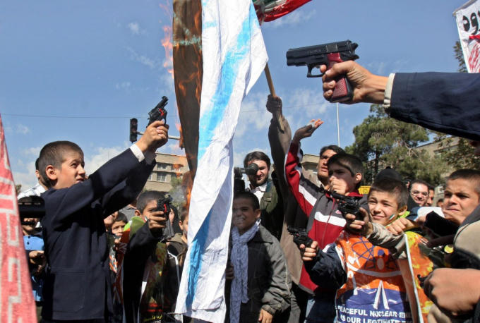 Các học sinh Iran bắn súng đồ chơi nhằm vào một lá cờ Israel đang bị đốt cháy trong một cuộc biểu tình chống Israel đánh dấu