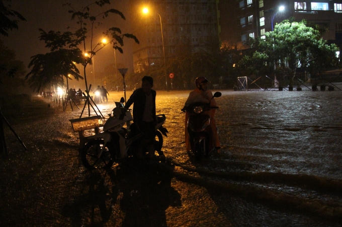 Nhiều bạn sinh viên không đi được nên chạy lên vỉa hè để chờ nước rút. Hai bạn nữ đang cố dắt xe máy để vào Kí túc xá. Do nước chảy mạnh nên phải một người dắt xe một người đi sau đẩy xe thì mới có thể thắng được dòng nước.