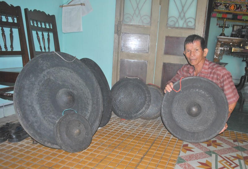 Ông Tại bên một bộ cồng chiêng năm xưa của làng Mỹ Thạnh. 