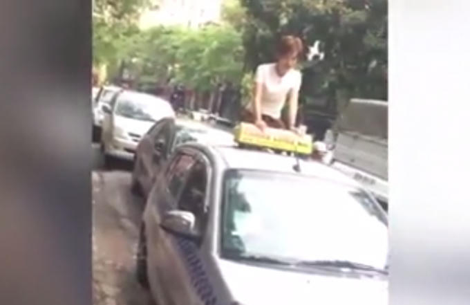 Hình ảnh cô gái leo lên ngồi trên nóc của một chiếc taxi khác.