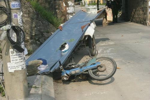 Chiếc xe máy kéo theo xe thô sơ chở tôn bị lật nhào. Ảnh: Võ Thạnh.