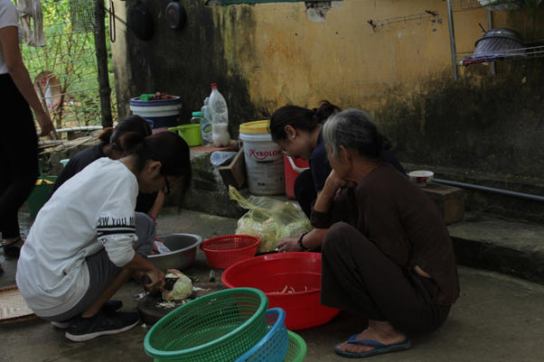 Cụ Nguyễn Thị Sợi (bệnh nhân phong), ngồi xem các bạn tình nguyện viên chuẩn bị đồ để nấu cơm.