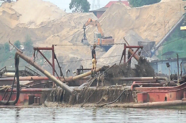 Sau khi dùng vòi rồng bơm hút cát lên tàu sẽ được sàng lọc để lấy cát đen, còn rác đổ lại xuống sông. (Ảnh: PV/Vietnam+).