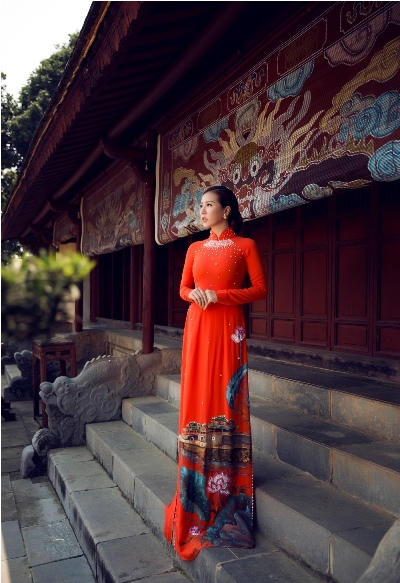 Trông cô thật rực rỡ trong tà áo dài màu cam đất vẽ hình đại nội huế, có đính kết hạt ngọc trai trên thân áo của NTk Brian Võ.