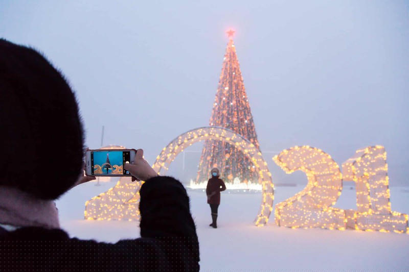 Một người tạo dáng chụp ảnh trước cây thông Noel được chiếu sáng và biển báo năm 2021.