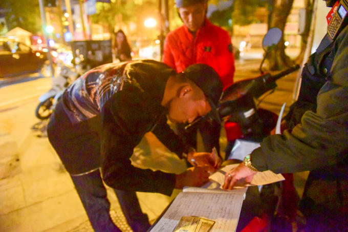 Người vi phạm giao thông ký vào biên bản phạt hành chính lỗi không đội mũ bảo hiểm.