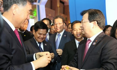 Phó thủ tướng Trịnh Đình Dũng (phải) mời Phó thủ tướng Trung Quốc Uông Dương, lãnh đạo các bộ, ngành và tỉnh Vân Nam thưởng thức vải thiều tại gian hàng nông sản Việt Nam. (Ảnh: VGP)