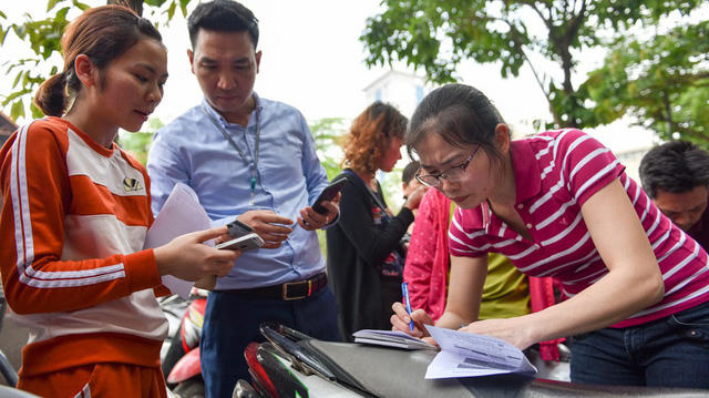 Nhiều người phải đợi tới 1, 2 tiếng đồng hồ vẫn chưa tới lượt. Tranh thủ lúc chờ tới lượt, khách hàng đứng điền thông tin vào tờ khai kê trên yên xe máy.
