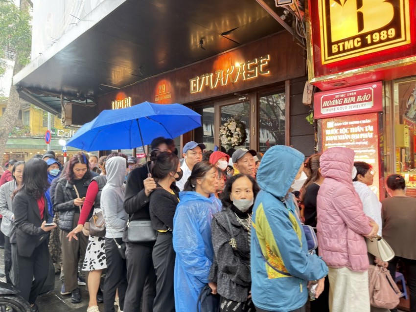 Người dân mặc áo mưa, che ô xếp hàng ngay ngắn chờ tới lượt mua vàng.