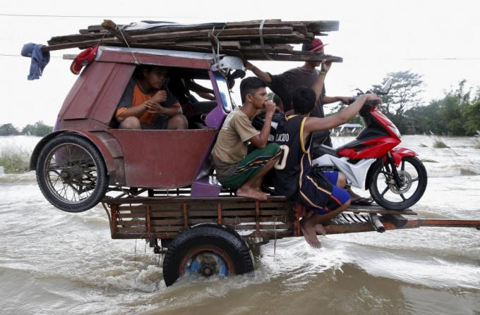 Người dân và phương tiện được một chiếc xe ba bánh chở đi qua những đoạn ngập nước do ảnh hưởng của một cơn bão đổ bộ vào miền bắc Philippines năm 2015. (Ảnh: Reuters)