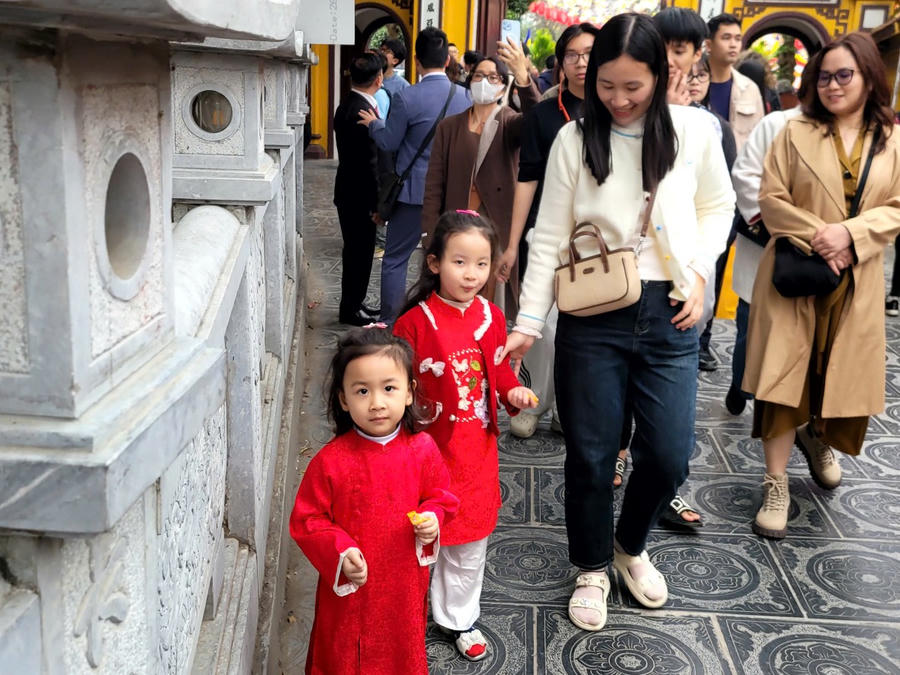 Gia đình đưa theo cả trẻ nhỏ, các bé diện những bộ áo dài truyền thống rực rỡ sắc màu, tò mò ngắm nhìn cảnh vật tại chùa. (Ảnh: Phạm Duy)