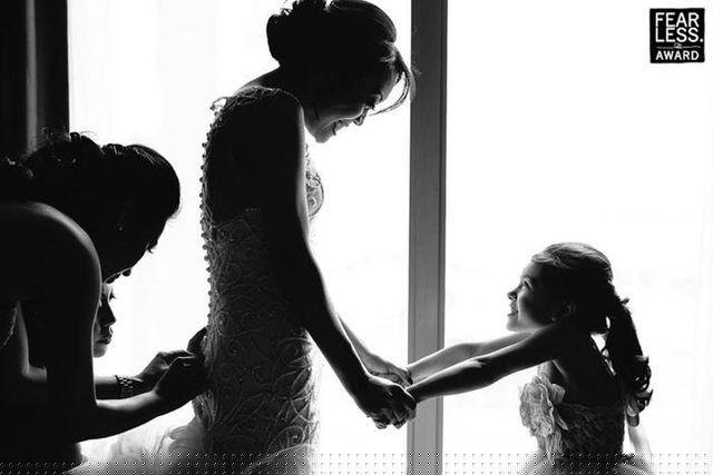 Một cô dâu đang nắm tay cô bé ôm hoa trong khi váy của cô đang được chỉnh sửa lại. Ảnh của nhiếp ảnh gia Allison Callaway chụp năm 2014.